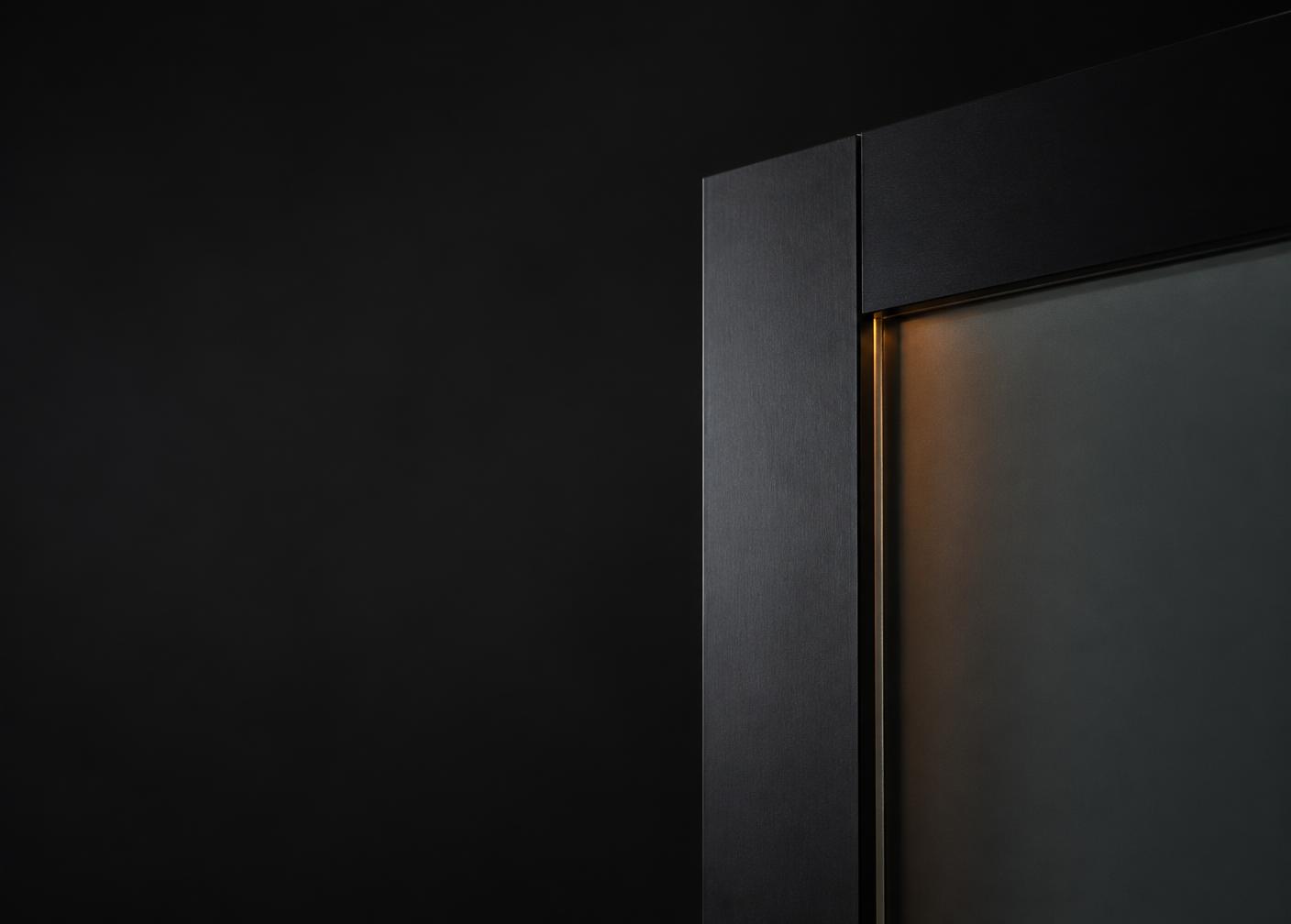 Brushed dark metal frame meeting frosted glass with a thin warm light line